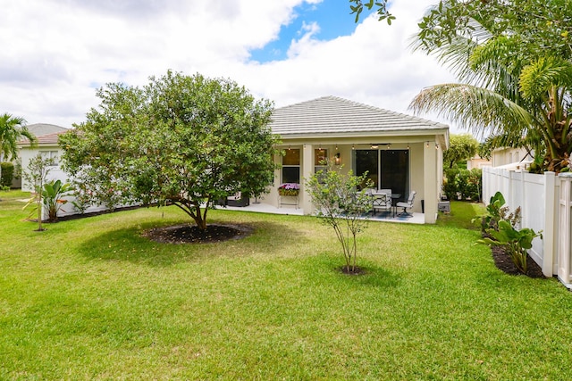rear view of house with ceiling fan, fence, a yard, a patio, and stucco siding