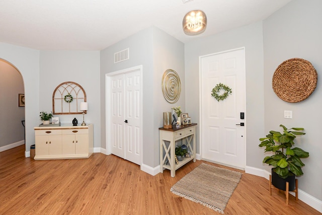 foyer entrance with visible vents, arched walkways, light wood-style flooring, and baseboards