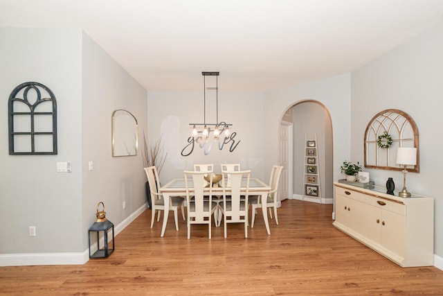 dining room featuring light wood-style floors, arched walkways, and baseboards