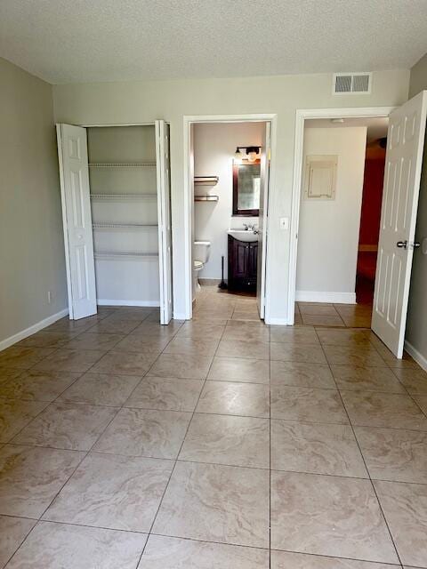 unfurnished bedroom with a textured ceiling, visible vents, a sink, and a closet
