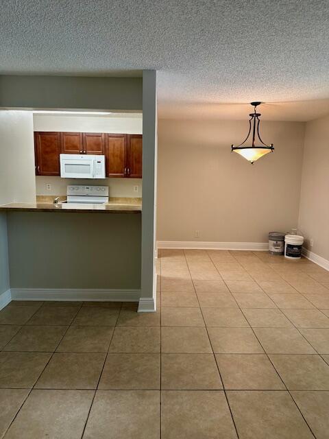 kitchen with a textured ceiling, hanging light fixtures, baseboards, white appliances, and light tile patterned flooring