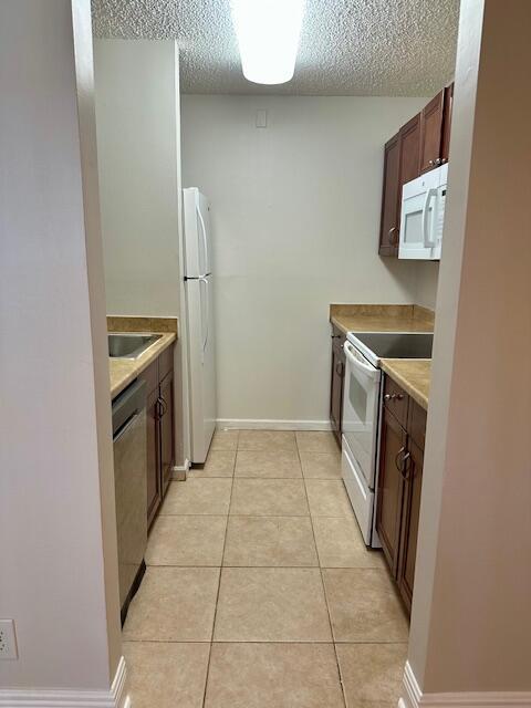kitchen with white appliances, light countertops, a textured ceiling, baseboards, and light tile patterned floors
