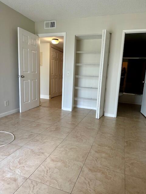unfurnished bedroom featuring light tile patterned floors, baseboards, a textured ceiling, and visible vents