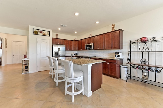 7384 NW Greenspring St, Port Saint Lucie, FL 34987 - kitchen with appliances with stainless steel finishes, a sink, decorative backsplash, light stone countertops, and a kitchen island with sink