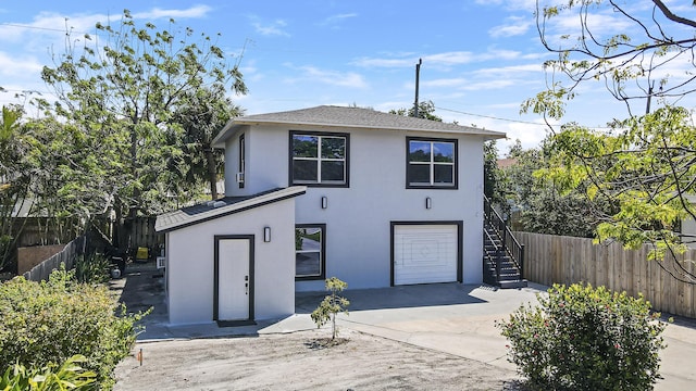 back of property featuring fence, stucco siding, concrete driveway, an attached garage, and stairway