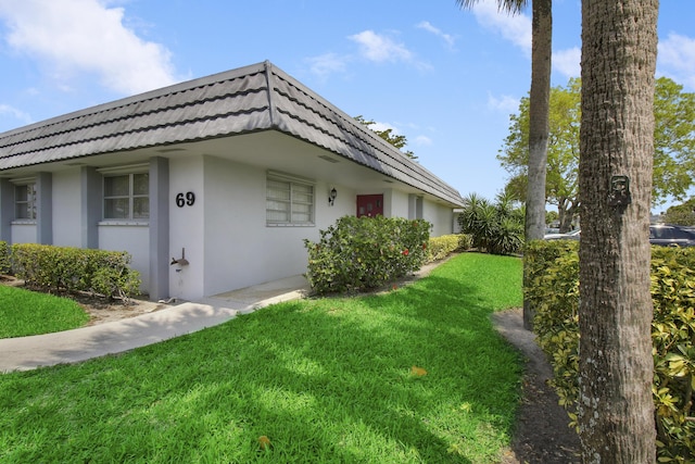 2886 Fernley Dr E Unit 69, West Palm Beach, FL 33415 - view of home's exterior featuring a tiled roof, mansard roof, stucco siding, and a yard