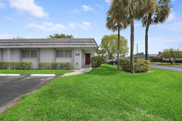 2886 Fernley Dr E Unit 69, West Palm Beach, FL 33415 - view of front facade featuring a tile roof, a front lawn, stucco siding, mansard roof, and uncovered parking