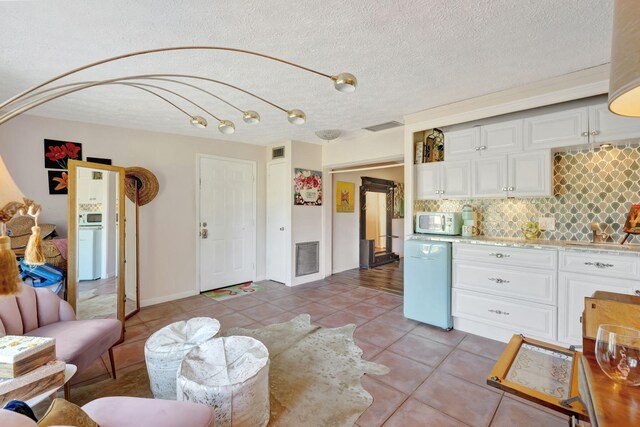 2971 SE Morningside Blvd, Port Saint Lucie, FL 34952 - kitchen with light countertops, white cabinetry, light tile patterned floors, white microwave, and backsplash