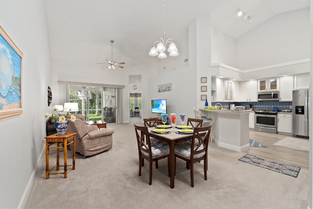 dining space with high vaulted ceiling, ceiling fan with notable chandelier, and light carpet