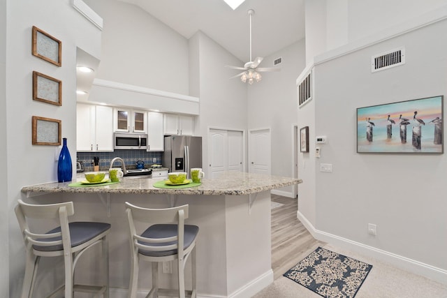 kitchen with visible vents, a peninsula, a kitchen breakfast bar, white cabinets, and appliances with stainless steel finishes