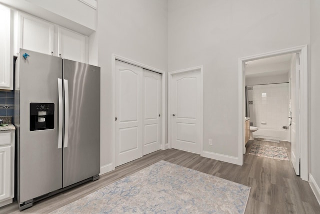 kitchen with stainless steel refrigerator with ice dispenser, baseboards, light wood-style floors, a high ceiling, and white cabinetry