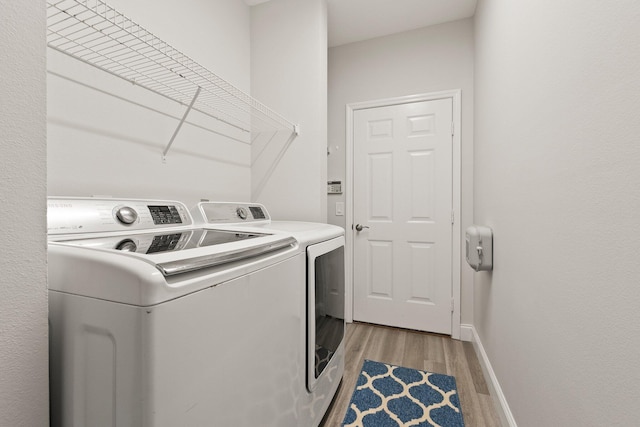 laundry room with laundry area, light wood finished floors, baseboards, and separate washer and dryer