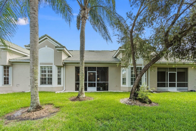 rear view of property featuring a sunroom, stucco siding, and a yard