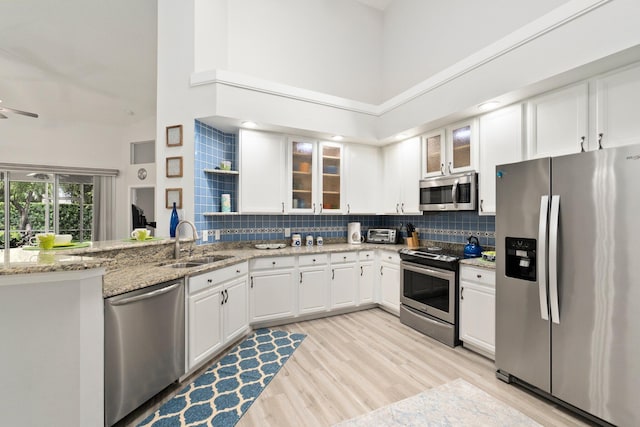 kitchen with high vaulted ceiling, white cabinetry, a sink, backsplash, and stainless steel appliances
