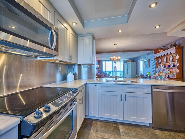 kitchen featuring a tray ceiling, pendant lighting, a sink, an inviting chandelier, and stainless steel appliances