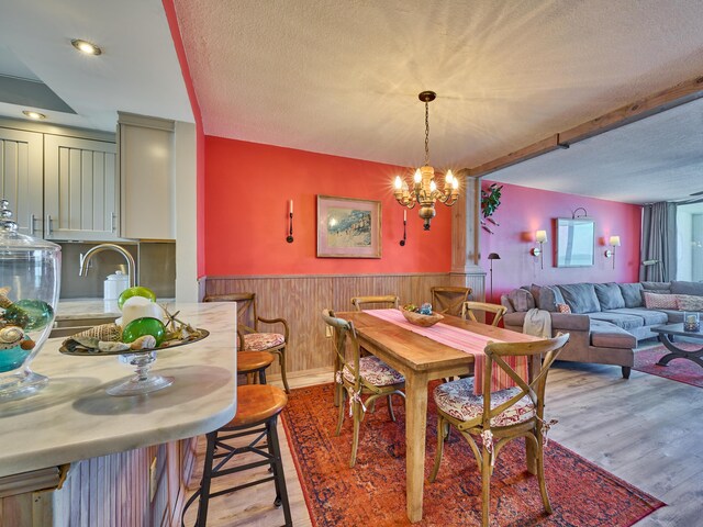 dining space with a textured ceiling, wood walls, a wainscoted wall, a notable chandelier, and light wood-style flooring