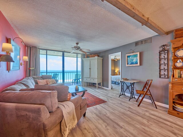 living area with visible vents, light wood-type flooring, a textured ceiling, a water view, and a ceiling fan