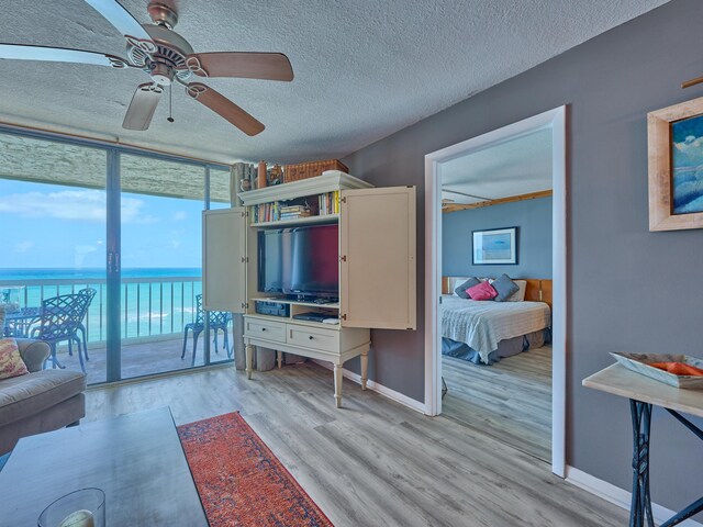living room with baseboards, floor to ceiling windows, a textured ceiling, a ceiling fan, and light wood-style flooring