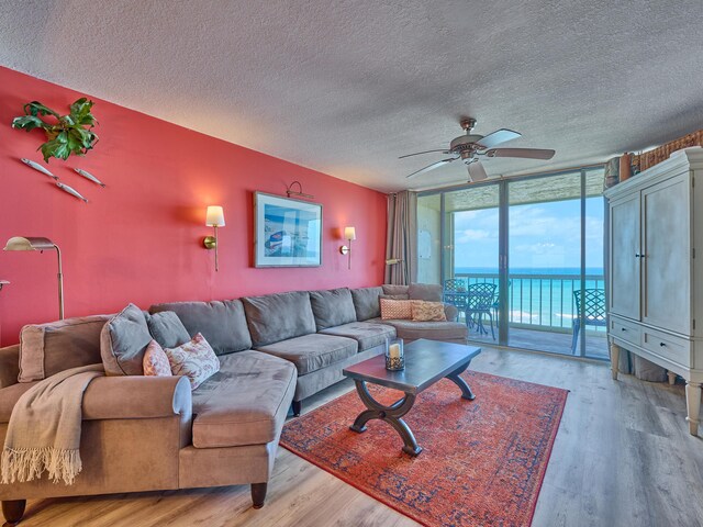 living area featuring a water view, a textured ceiling, floor to ceiling windows, and light wood-style flooring