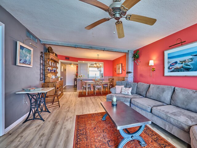 living room with a textured ceiling, ceiling fan with notable chandelier, baseboards, wood finished floors, and visible vents