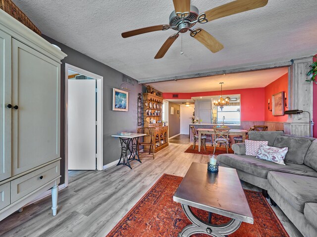living room with a textured ceiling, ceiling fan with notable chandelier, and light wood-style floors