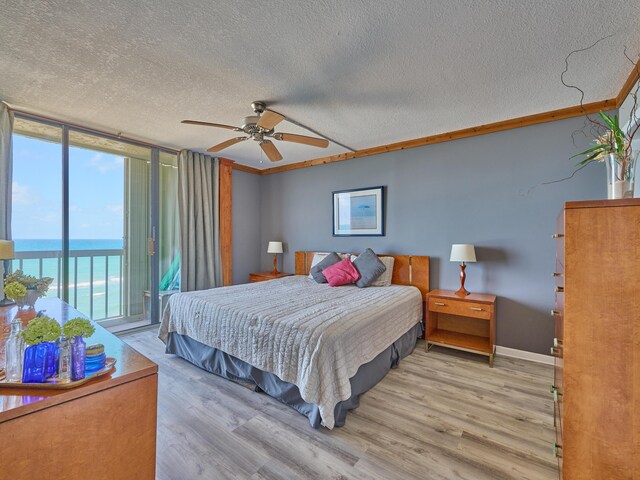 bedroom with access to outside, a textured ceiling, light wood-type flooring, a water view, and floor to ceiling windows