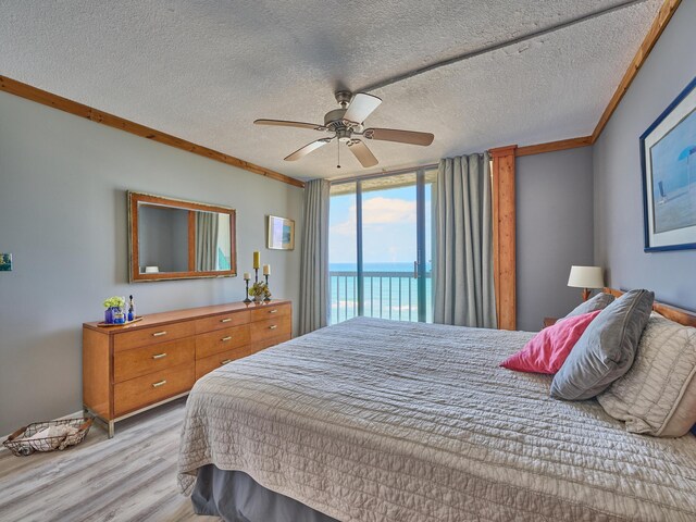bedroom featuring crown molding, a textured ceiling, light wood-style flooring, and a water view