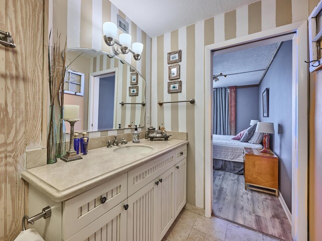 ensuite bathroom featuring vanity, baseboards, wallpapered walls, connected bathroom, and a textured ceiling
