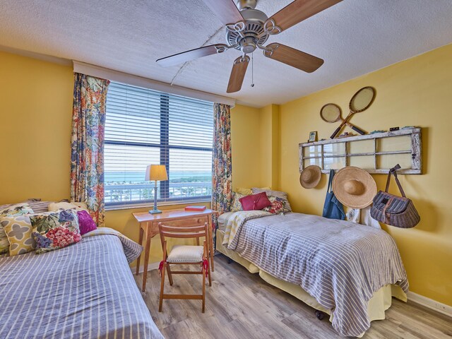 bedroom featuring baseboards, a textured ceiling, ceiling fan, and wood finished floors