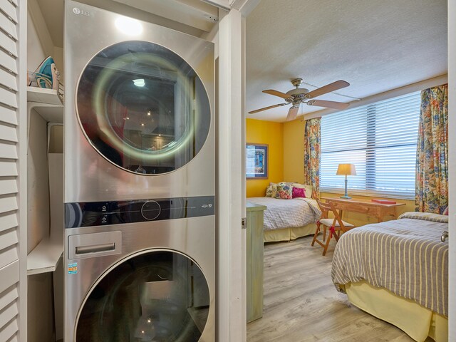 clothes washing area with laundry area, a textured ceiling, a ceiling fan, stacked washer / dryer, and wood finished floors
