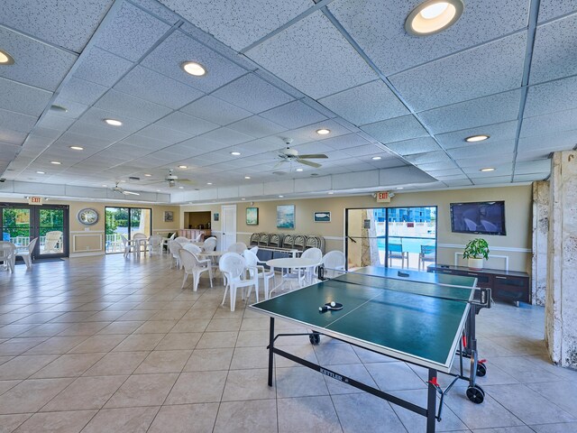 rec room with a paneled ceiling, ceiling fan, and light tile patterned floors