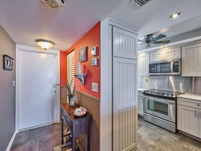 kitchen featuring ceiling fan, visible vents, light countertops, a wainscoted wall, and stainless steel appliances