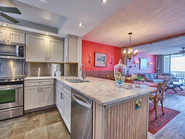 kitchen with a peninsula, ceiling fan with notable chandelier, open floor plan, a sink, and appliances with stainless steel finishes