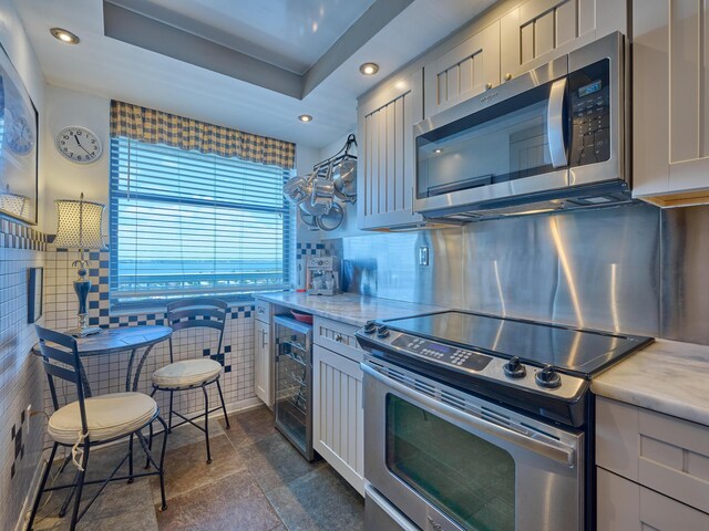 kitchen featuring appliances with stainless steel finishes, light stone counters, beverage cooler, recessed lighting, and decorative backsplash