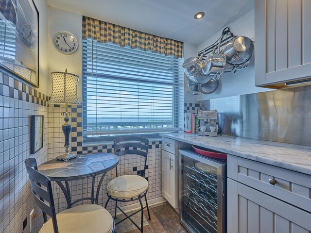 kitchen featuring beverage cooler, recessed lighting, light stone counters, and tile walls