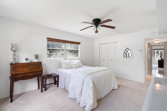 bedroom featuring a closet, baseboards, light colored carpet, a textured ceiling, and a ceiling fan