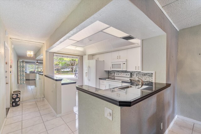 kitchen featuring a textured ceiling, visible vents, white cabinets, a peninsula, and white appliances