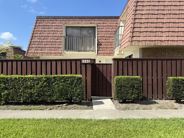view of front facade with a gate, fence, mansard roof, and brick siding