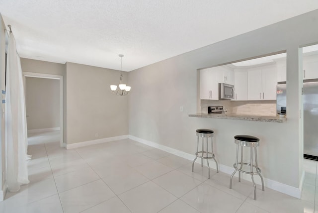 kitchen featuring white cabinets, an inviting chandelier, stainless steel appliances, decorative light fixtures, and a kitchen bar