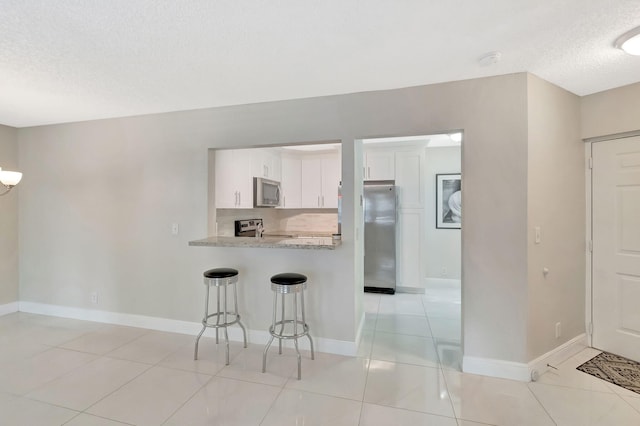 kitchen featuring a kitchen bar, a textured ceiling, light countertops, white cabinets, and stainless steel appliances