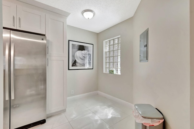interior space with a textured ceiling, baseboards, light tile patterned flooring, and electric panel