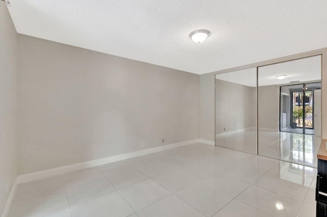 empty room with baseboards, light tile patterned flooring, and a textured ceiling