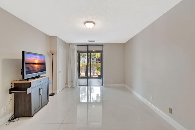 unfurnished living room featuring baseboards, a textured ceiling, light tile patterned flooring, and visible vents