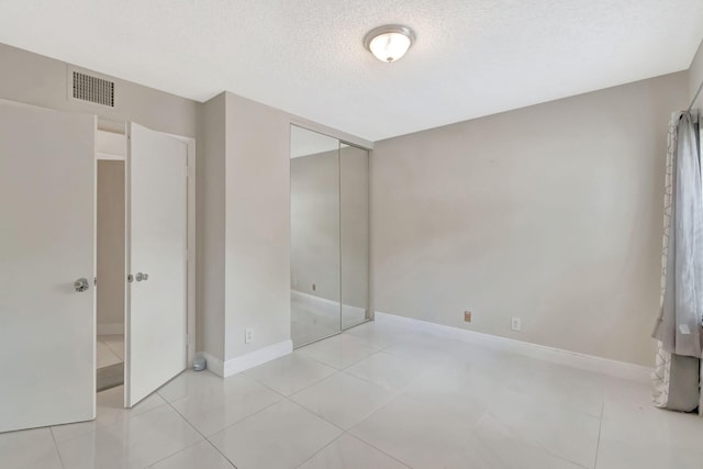 unfurnished bedroom featuring visible vents, a closet, baseboards, a textured ceiling, and tile patterned floors