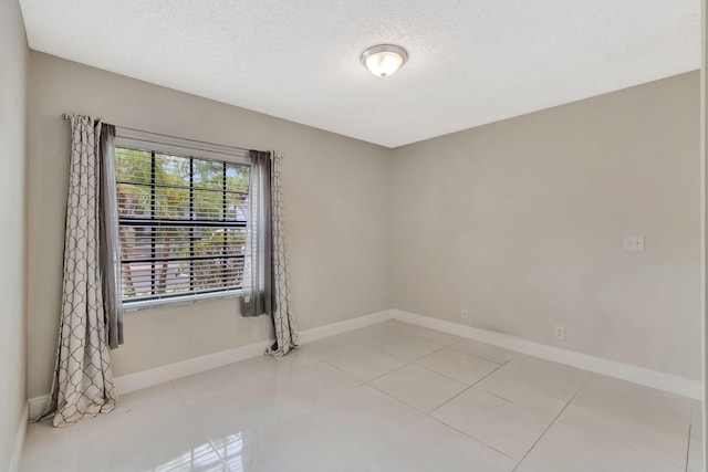 empty room featuring baseboards, a textured ceiling, and light tile patterned floors