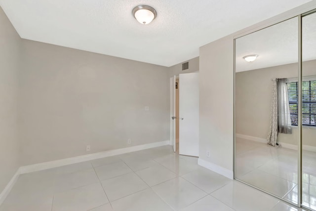 spare room with light tile patterned floors, a textured ceiling, visible vents, and baseboards