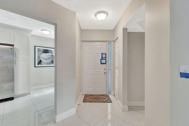 foyer entrance featuring light tile patterned flooring, a textured ceiling, and baseboards