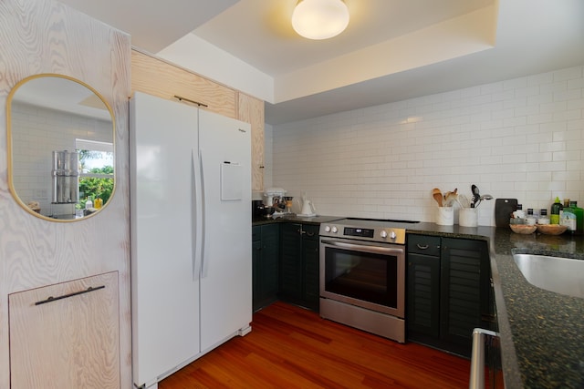 kitchen featuring freestanding refrigerator, dark wood-style flooring, dark stone counters, stainless steel electric stove, and tasteful backsplash