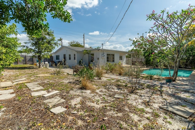 rear view of property featuring fence, an outdoor pool, and stucco siding