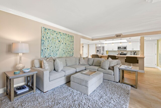 living area featuring crown molding, baseboards, light wood-type flooring, and visible vents